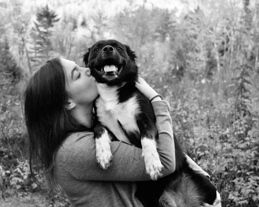 photo en noir et blanc : une femme elbrasse le chien de berger qu'elle tient dans ses bras